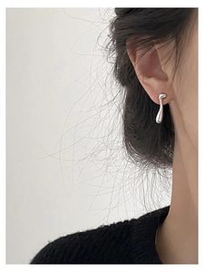 Detailed close-up of a silver asymmetric water drop earring worn by a model in a modern style