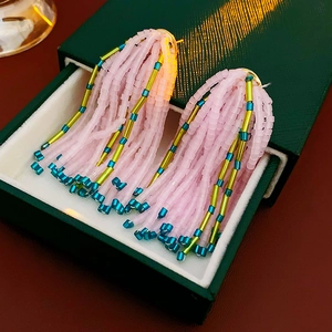 Détail macro de boucles d'oreilles à pompon en perles roses et dorées dans un écrin vert