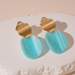 Détail de boucles d'oreilles en métal doré et résine bleu-vert sur socle en pierre