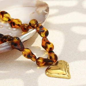 Macro shot of 18K gold heart pendant with leopard print amber resin beads on natural shell