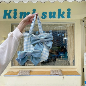 Detail of blue plaid canvas tote bag with large denim bows held in hand at a cafe