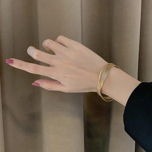 Bracciale rigido incrociato in oro opaco minimalista indossato per un look chic