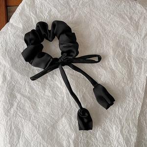 Detail of black satin scrunchie featuring elegant ribbon and tulip flower pendant
