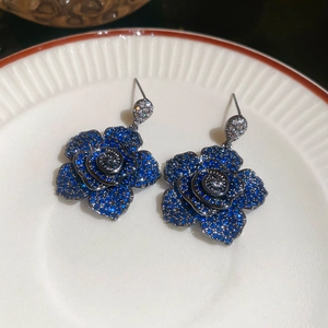 Macro detail of blue crystal encrusted rose drop earrings on a white ceramic plate