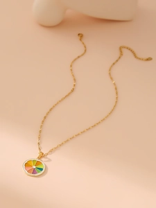 Detail of golden fruit necklace with colorful enamel pendant over a soft pink backdrop
