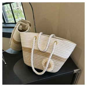 Detail of hand-woven straw tote bag featuring a large white floral accent and rope handles