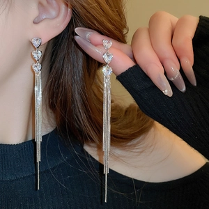 Detail of silver long tassel earrings with three linked rhinestone hearts on model