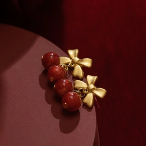 Macro shot of matte gold bow earrings with polished red resin bead pendants for women