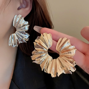 Macro shot of large pleated fan-shaped metal earrings in gold and silver finish