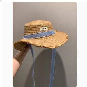 Detail of straw sun hat featuring light blue plaid ribbon and natural frayed edge
