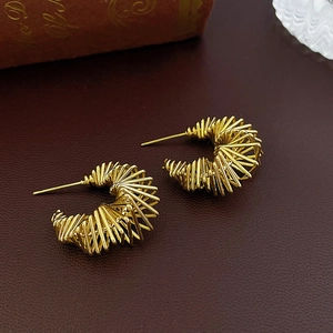 Close-up of golden irregular layered C-shaped metal hoop earrings on leather background