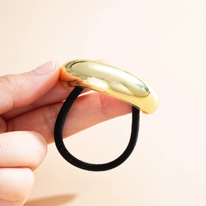 Detail of hand holding a black elastic hair tie with a polished gold curved metal accent