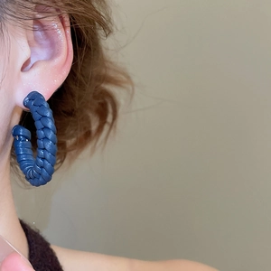 Detailed view of a navy blue hand-woven leather C-shaped hoop earring on a model