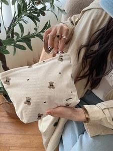 Cute beige corduroy makeup bag with embroidered bear and hearts held by a model