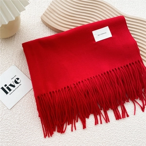 Detail of red tassel scarf with minimalist brand label on a cozy aesthetic background