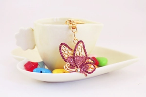 Macro shot of rose pink rhinestone and white pearl butterfly keychain on a white tea cup