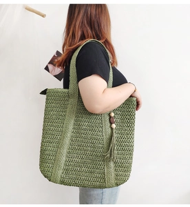 Detail of green straw tote bag featuring decorative tassels and wooden bead accents