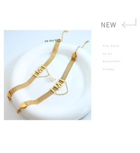 Close-up of gold mesh choker featuring a large letter M charm and a single white pearl