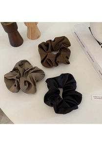 Close-up of three satin scrunchies in black, dark brown, and taupe on a minimalist surface
