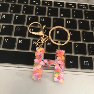 Close-up of letter H keychain with colorful heart glitter on a black keyboard