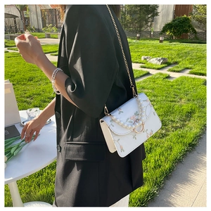 Detail of floral embroidery on white handbag with pearl handle and gold ring clasp