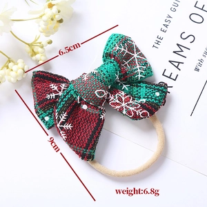 Detailed view of red and green plaid Christmas bow headband with white snowflake patterns
