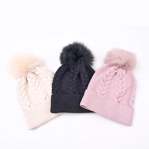 Trois bonnets tricotés à pompon en blanc, noir et rose avec des textures torsadées