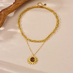 Gold layered sun pendant necklace with tiger eye stone on textured sandy background