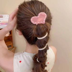 Vue détaillée d'une pince à cheveux cœur rose et d'un élastique spirale blanc en coiffure