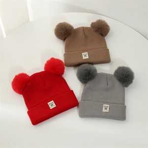 Flat lay of knit baby beanies in brown, red, and grey with dual pom poms and cloth labels