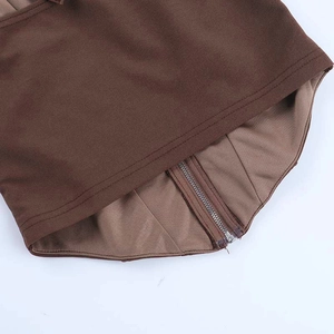Detailopname van de bruine haltertop met gebogen zoom, precieze stiksels en metalen ritssluiting