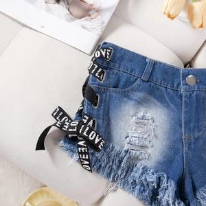 Dettaglio di orlo sfilacciato, anelli in metallo e nastro LOVE su shorts di jeans
