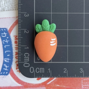 Detail view of mini resin carrot charm with green leaves on measuring scale grid