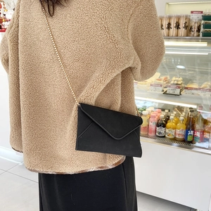 Minimalist black envelope bag with gold chain strap worn as a stylish shoulder bag
