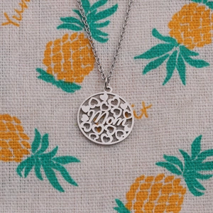 Détail du collier argenté avec pendentif MOM et motifs de cœur sur fond décoré
