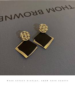 Detail of geometric drop earrings featuring golden mesh circles and black square layers