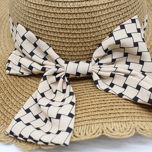 Macro view of woven straw sun hat featuring a geometric patterned beige fabric bow
