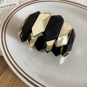 Close-up of geometric black and gold stretch bracelet on a white ceramic tray