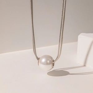 Macro detail of a 18K gold plated snake chain necklace with a large round white pearl