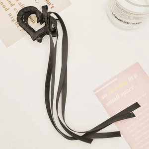 Dettaglio di una pinza per capelli a cuore nera con lunghi nastri su sfondo bianco