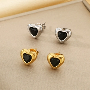 Macro shot of gold and silver heart studs with black gemstones on a textured surface