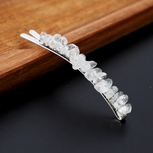 Macro shot of natural clear crystal hair clip on dark wooden tray with metal base