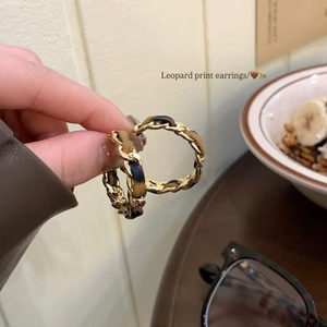 Detail of leopard print woven gold chain hoop earrings held by hand in a warm setting