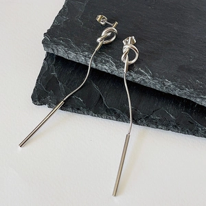 Macro shot of silver knot earrings with long snake chains and solid metal rods on slate