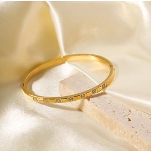 Detailed shot of gold-plated bangle with white zircon inlays on premium champagne satin cloth