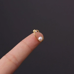 Close-up of golden C-shaped cartilage stud with white pearl and small zircon on a fingertip