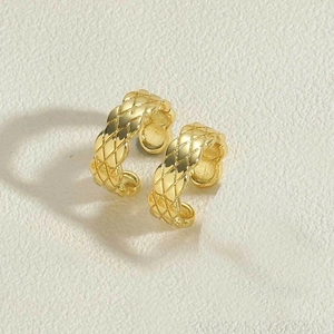 Macro detail of gold-plated quilted pattern C-shaped cuff earring on stone surface