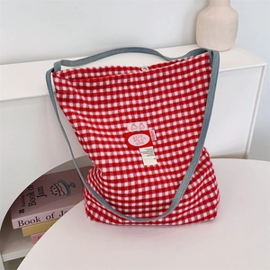 Detail of red and white plaid tote bag with denim strap and cherry label on a white table