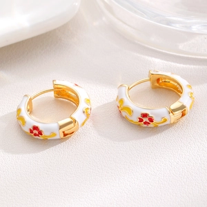 Detail of gold enamel hoop earrings featuring white base and red flower patterns