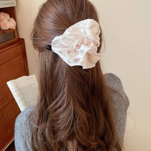 Détail macro d'une pince à cheveux en satin plissé crème portée sur les cheveux